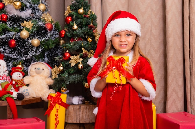 Nettes kleines kaukasisches Mädchen, das zu Hause für Weihnachten gekleidet ist und ein Geschenk hält.