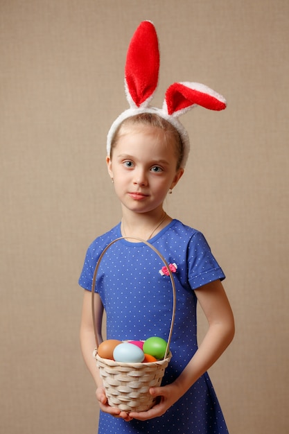 Nettes kleines Kind, das Hasenohren am Ostertag trägt. Mädchen, das Korb mit gemalten Eiern hält.