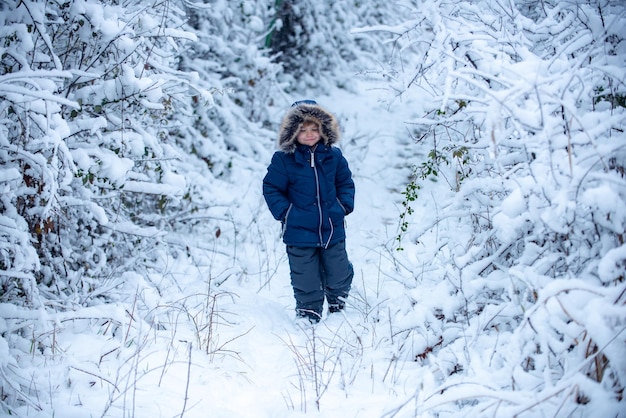 Nettes kleines Kind, das im Winterpark im Schnee genießt Kinder, die Spaß im weißen Schneefeld gegen Schnee haben