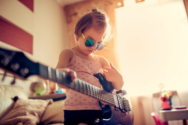 Nettes kleines Kindermädchen in der Sonnenbrille, die Gitarre spielt.