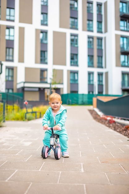 Nettes kleines Kleinkindmädchen in blauen Overalls, das auf Laufrad reitet, glückliches gesundes schönes Baby...