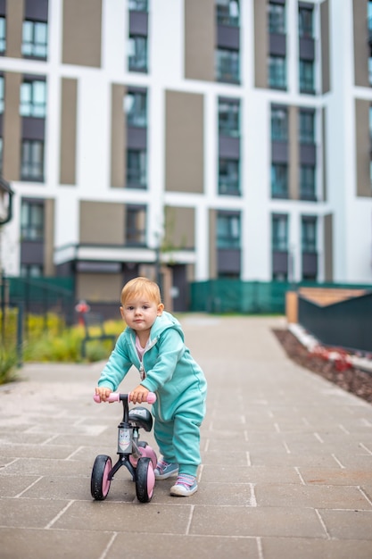 Nettes kleines Kleinkindmädchen in blauen Overalls, das auf Laufrad reitet, glückliches gesundes schönes Babykind...