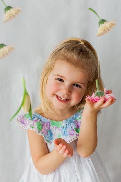 Nettes kleines Mädchen 3 Jahre alt mit blonden Haaren mit farbigen Blumen auf weißem Hintergrund Frühlingsferien Glückliches Kind