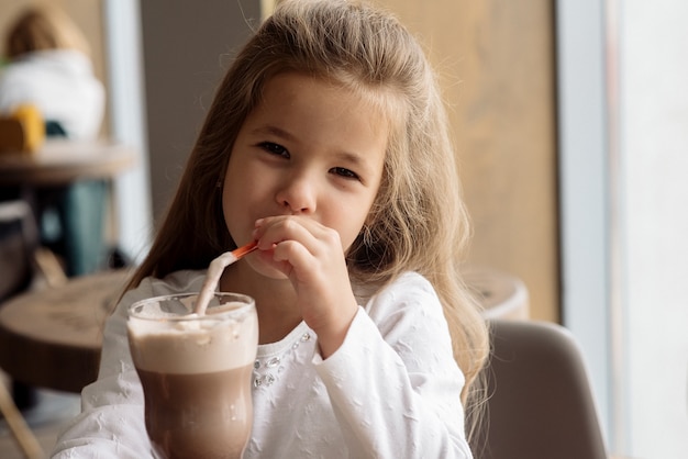 Nettes kleines Mädchen 5 Jahre alt trinkt Kakao in einem Café