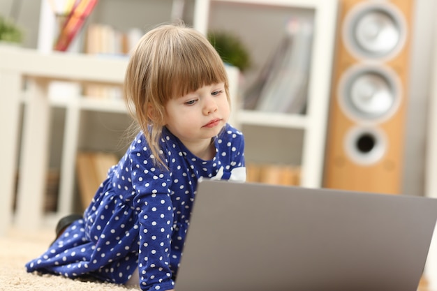 Nettes kleines Mädchen auf Bodenteppichgebrauchs-Laptop-PC für Chat mit ihrem Vati weg auf Geschäftsporträt. Zeigen Sie Fingerhand im drahtlosen IP-Telefoniekonzept des Anzeigensozialnetz-Bankhypothekenkredits