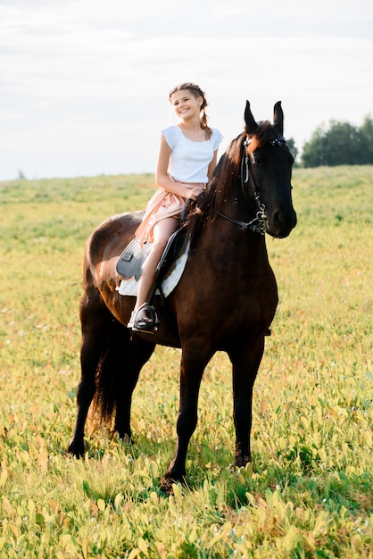 Nettes kleines Mädchen auf einem Pferd in einem Sommerfeldkleid