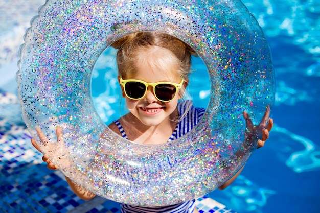 Nettes kleines Mädchen Blondine in Sonnenbrille lacht im Pool mit einer Rettungsleine