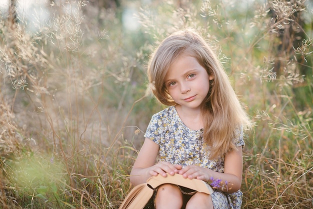 Nettes kleines Mädchen, das auf dem Gras sitzt und ein Buch darin liest