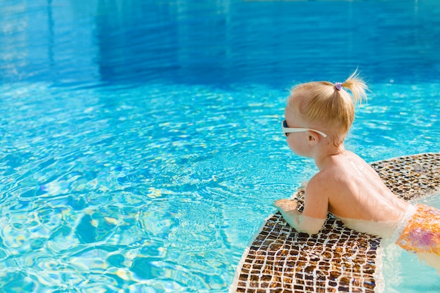 Nettes kleines Mädchen, das auf der Seite des Pools liegt und das blaue Wasser betrachtet. Ansicht von oben. Kopieren Sie Platz.