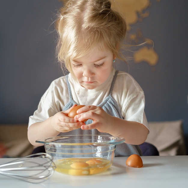 Nettes kleines Mädchen, das beim Kochen mit Mama Eier in eine Schüssel bricht