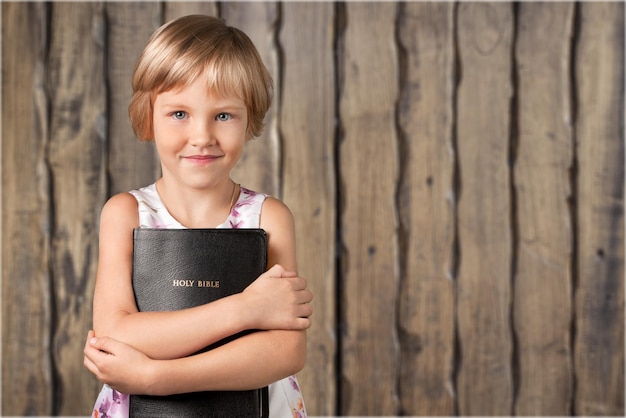Nettes kleines Mädchen, das Bibel im Hintergrund hält