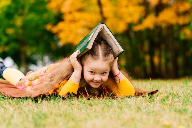 Nettes kleines Mädchen, das ein Buch im Herbstpark liest