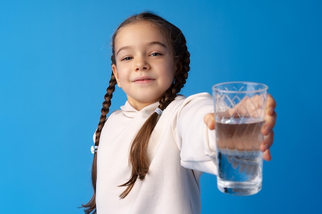 Nettes kleines Mädchen, das ein Glas Wasser auf blauem Hintergrund hält