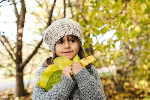 Nettes kleines Mädchen, das gelbe Ahornblätter in ihren Händen hält, während es im sonnigen Park im Herbst spazieren geht Porträt eines kleinen Mädchens, das während der Laubzeit im Park oder Wald steht Kindheit und Spaziergänge in der Natur