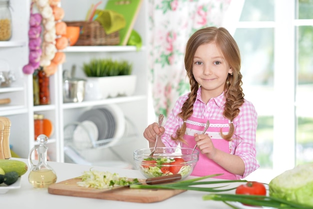 Nettes kleines Mädchen, das Gemüsesalat in der Küche zubereitet