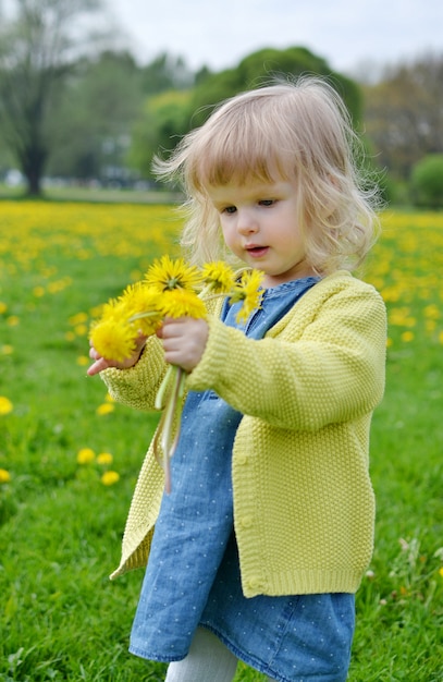 Nettes kleines Mädchen, das im Park mit Löwenzahnblumen geht