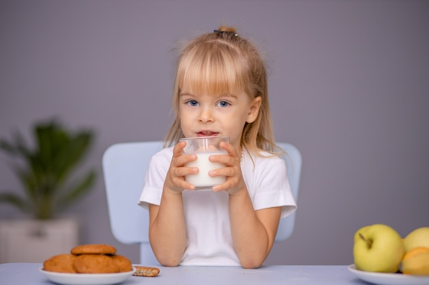 Nettes kleines Mädchen, das Kekse isst und Milch zu Hause oder im Kindergarten trinkt