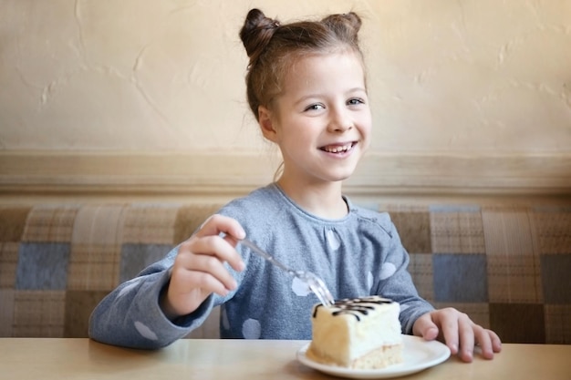 Nettes kleines Mädchen, das leckeren Kuchen in der Küche isst