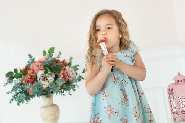 Nettes kleines Mädchen, das Make-up anwendet, das in Spiegel schaut. Kleines Fashionista-Mädchen, das mit der Kosmetik ihrer Mutter spielt. Entzückendes Kind drinnen