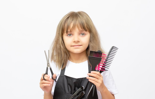 Nettes kleines Mädchen, das mit einem Haarbürstenfriseur auf weißem Hintergrund spielt