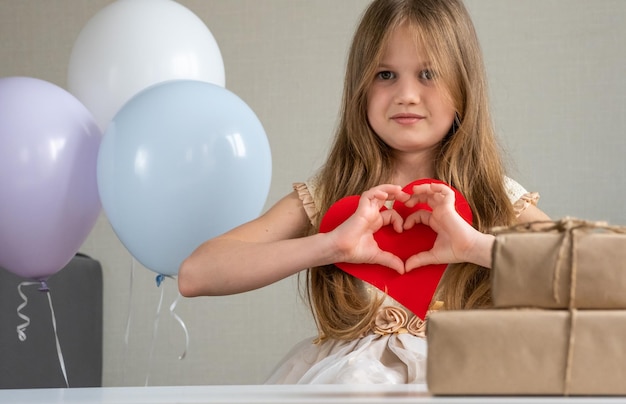 Nettes kleines Mädchen, das mit ihren Händen Herz macht und lächelnd Mutter am Muttertag gratuliert