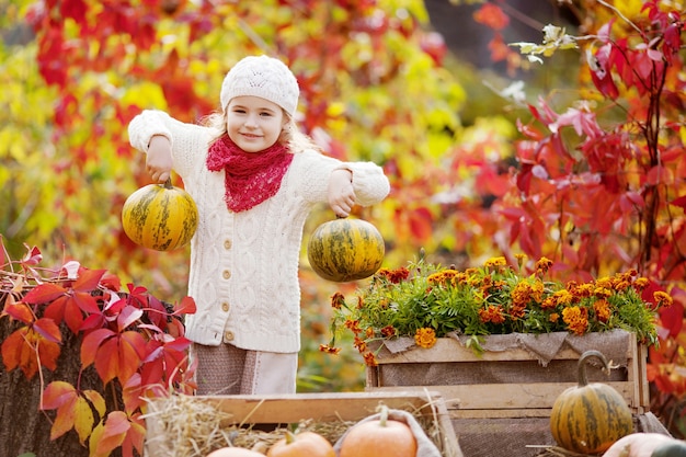 Nettes kleines Mädchen, das mit Kürbissen im Herbstpark spielt. Herbstaktivitäten für Kinder. Halloween- und Thanksgiving-Zeitspaß für die Familie.