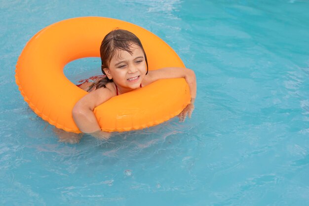 Nettes kleines Mädchen, das orangefarbenen aufblasbaren Schwimmer im Swimmingpool verwendet, genießt glücklich den Urlaub