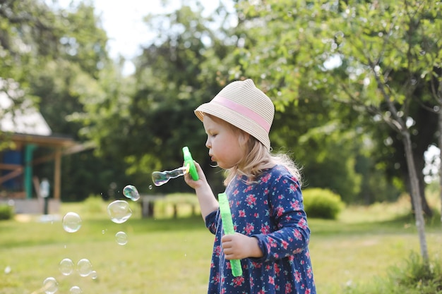 Nettes kleines Mädchen, das Seifenblasen auf einem Spaziergang im Sommer im Freien bläst