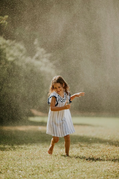 Nettes kleines Mädchen, das Spaß mit Wasser unter Bewässerungssprinkler hat