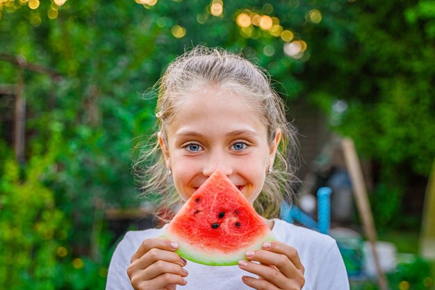 Nettes kleines Mädchen, das Wassermelone im grünen Garten isst