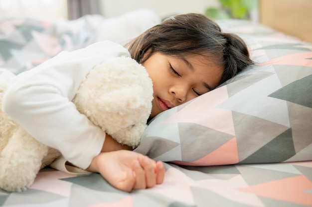 Nettes kleines Mädchen, das zu Hause auf dem Bett mit weichen Kissen schläft