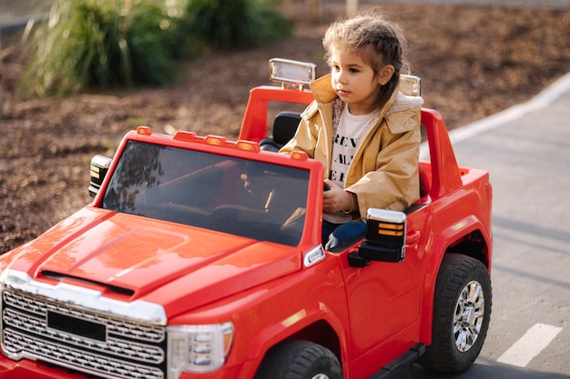 Nettes kleines Mädchen fährt in einer Mini-Stadt auf einem roten Elektroauto-Jeep. Entzückende kleine Mädchenstraße in Spielzeug