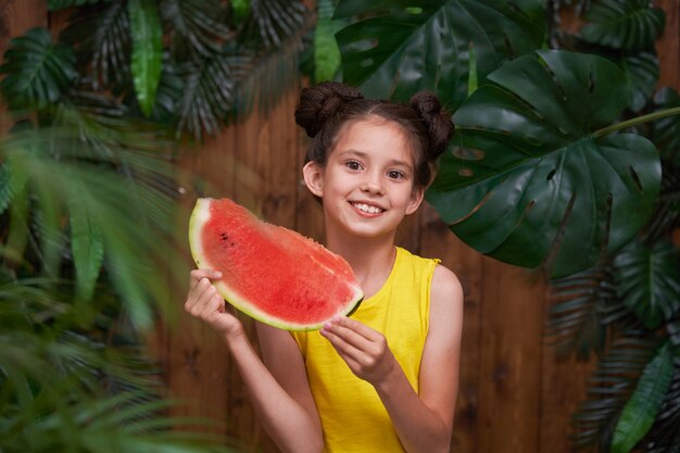 Nettes kleines Mädchen, fröhlich lachend und ein Stück Wassermelone in ihren Händen haltend