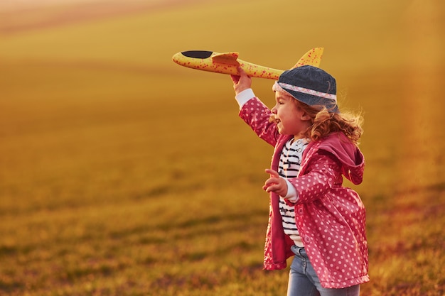 Nettes kleines Mädchen haben Spaß mit Spielzeugflugzeug auf dem schönen Feld am sonnigen Tag