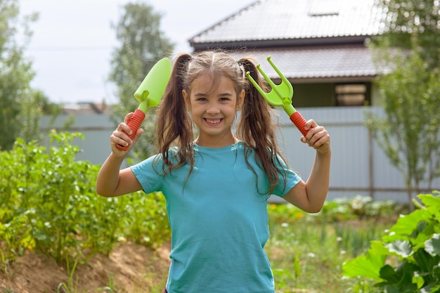 Nettes kleines Mädchen hält kleine Gartengeräte im Garten