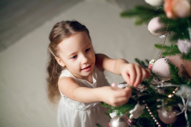 Nettes kleines Mädchen im Kleid, das Weihnachtsbaum verziert. Neujahr.