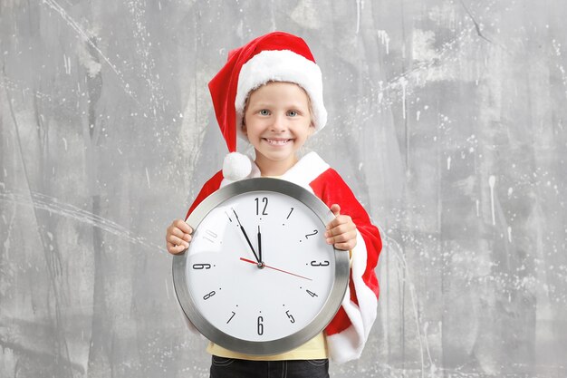 Nettes kleines Mädchen im Weihnachtsmann-Anzug mit Uhr auf Schmutzoberfläche