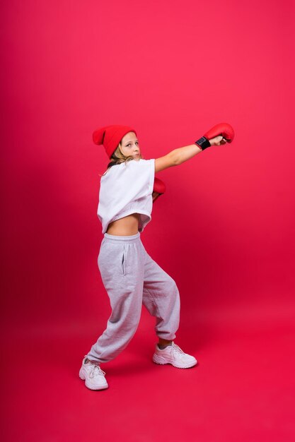 Nettes kleines Mädchen in den Boxhandschuhen auf rotem Hintergrundstudio