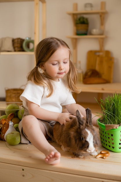 Nettes kleines Mädchen in der Holzküche des Hauses füttert das Kaninchen frisches Gras