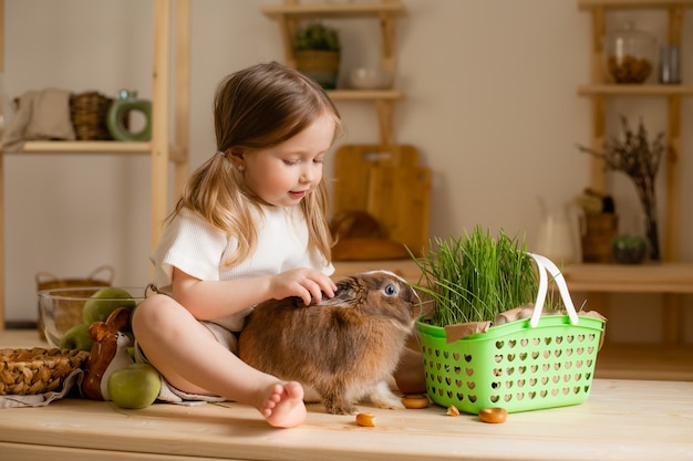 Nettes kleines Mädchen in der Holzküche des Hauses füttert das Kaninchen frisches Gras