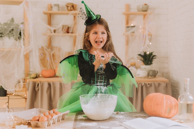 Nettes kleines Mädchen in einem grünen Halloween-Kostüm einer Hexe oder Fee bereitet einen Kürbiskuchen vor