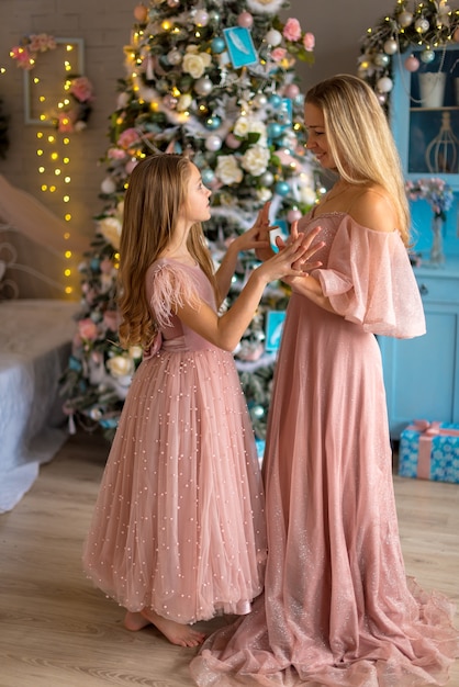 Nettes kleines Mädchen in einem rosa Kleid mit ihrer Mutter an Weihnachten