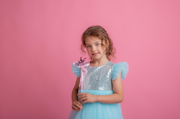 Nettes kleines Mädchen in einem schönen Kleid, das einen feenhaften Zauberstab auf einem rosa Hintergrund hält