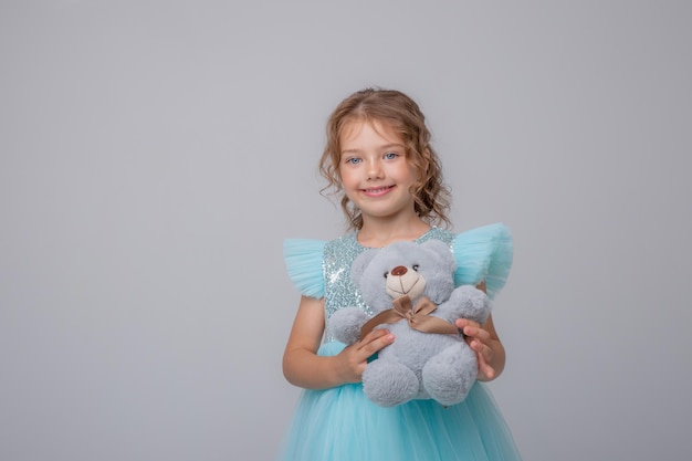 Nettes kleines Mädchen in einem schönen Kleid, das einen Teddybären auf einem weißen Hintergrund hält