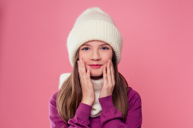 Nettes kleines Mädchen in warmer Strickmütze auf rosa Hintergrund im Studio. Kinder Winterkleidung.