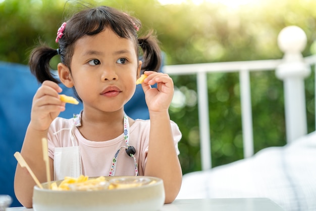 Nettes kleines Mädchen isst gerne Pommes zum Mittagessen im Freien