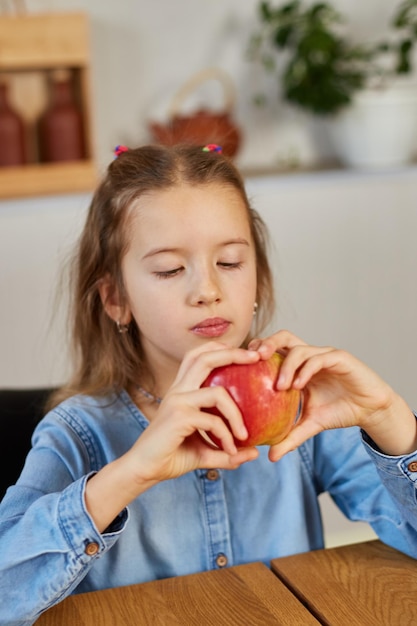 Nettes kleines Mädchen isst zu Hause roten Apfel im Kücheninnenraum