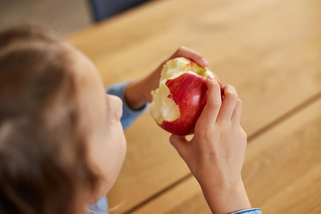 Nettes kleines Mädchen isst zu Hause roten Apfel im Kücheninnenraum