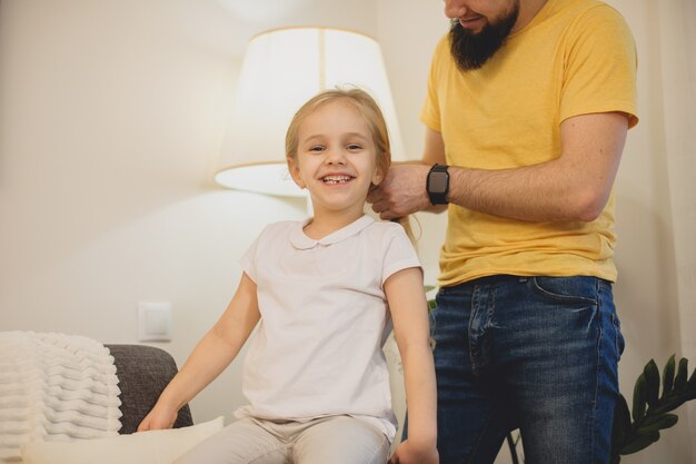 Nettes kleines Mädchen lacht und während ihr Vater ihre Haare zu Hause arrangiert