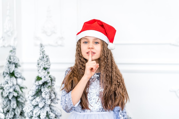 Nettes kleines Mädchen macht Stille Geste neben Weihnachtsschmuck